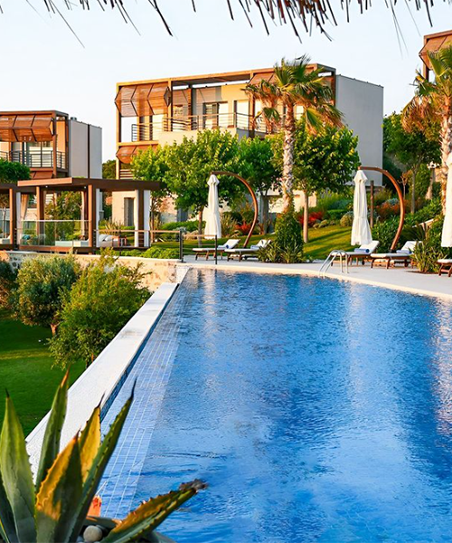 Yemyeşil bahçeler ve palmiye ağaçları ile çevrili modern mimariye sahip, ahşap detaylı otel binalarının önünde uzanan masmavi bir sonsuzluk havuzu, beyaz şemsiyeler ve şezlonglarla birlikte Bodrum'un en iyi otellerinden birinde huzurlu bir konaklama deneyimi sunuyor.