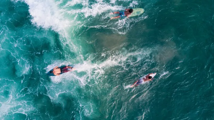 Bali’de Canggu sahilinde okyanus dalgalarında sörf yapan sporcular ve turistik sörf dersi alan ziyaretçiler