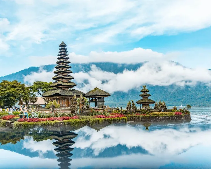 Bali’de göl kenarında yer alan Tanah Lot Tapınağı’nın bulutlar ve dağ manzarasıyla yansıdığı tropik manzara