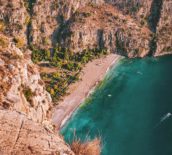 Fethiye'deki Kabak Koyu'nun kuşbakışı görüntüsü, turkuaz renkteki denizi, dik yamaçlarla çevrili kumsalı ve yeşillikler içindeki kamp alanlarıyla Türkiye'nin en iyi kamp rotaları arasında doğa harikası bir destinasyonu gözler önüne seriyor.