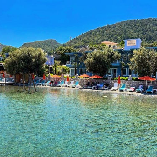 Fiska otelin önündeki berrak ve sığ Selimiye denizi, sahilde sıralanmış renkli şezlonglar ve turuncu şemsiyelerin altında güneşlenen tatilcilerle, yemyeşil tepelerin gölgesinde huzurlu bir Güney Ege tatil köyü atmosferi sunuyor.