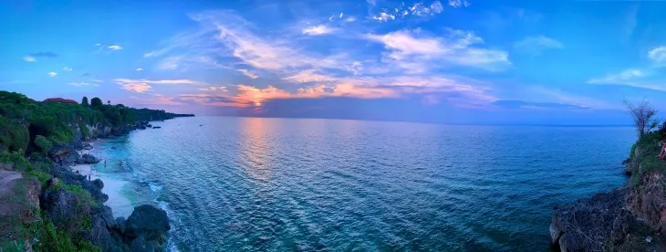 Bali’de Jimbaran Bay plajında gün batımı sırasında turuncu ve mavi tonlara bürünen okyanus manzarası