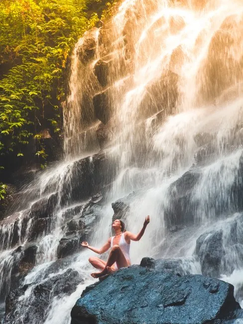 Bali’nin Gianyar köyündeki Kanto Lampo Şelalesi’nde kayalar üzerinde meditasyon yapan ziyaretçi ve tropik bitki örtüsü