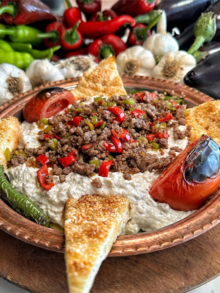 Bakır tepside servis edilen, közlenmiş patlıcan ezmesi üzerinde renkli biberlerle harmanlanmış kıymalı harcın, közlenmiş domates ve biberlerin ve susamlı pide üçgenlerinin bir araya geldiği bu eşsiz sunum, Antalya'nın en iyi restoranlarında tadabileceğiniz zengin Türk mutfağı lezzetlerini yansıtıyor.