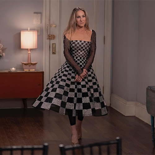 And Just Like That dizisinin öne çıkan kostümleri arasında yer alan, Sarah Jessica Parker'ın canlandırdığı Carrie Bradshaw'ın siyah-beyaz damalı, ışıltılı ve kabarık etekli, transparan kollu elbisesiyle iç mekanda düşünceli bir ifadeyle duruşu, karakterin eklektik stilini gözler önüne seriyor.