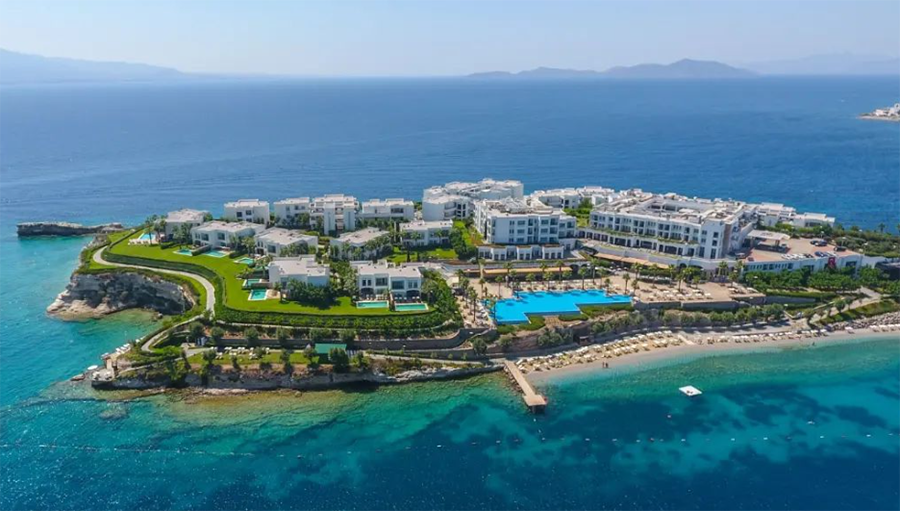 Bodrum'un en iyi otellerinden Xanadu Island'ın masmavi Ege Denizi'nde, özel bir yarımada üzerine kurulmuş, bembeyaz modern yapıları, yemyeşil peyzajlı alanları, birden fazla berrak sonsuzluk havuzu ve uzun özel plajıyla göz alıcı kuşbakışı görüntüsü.