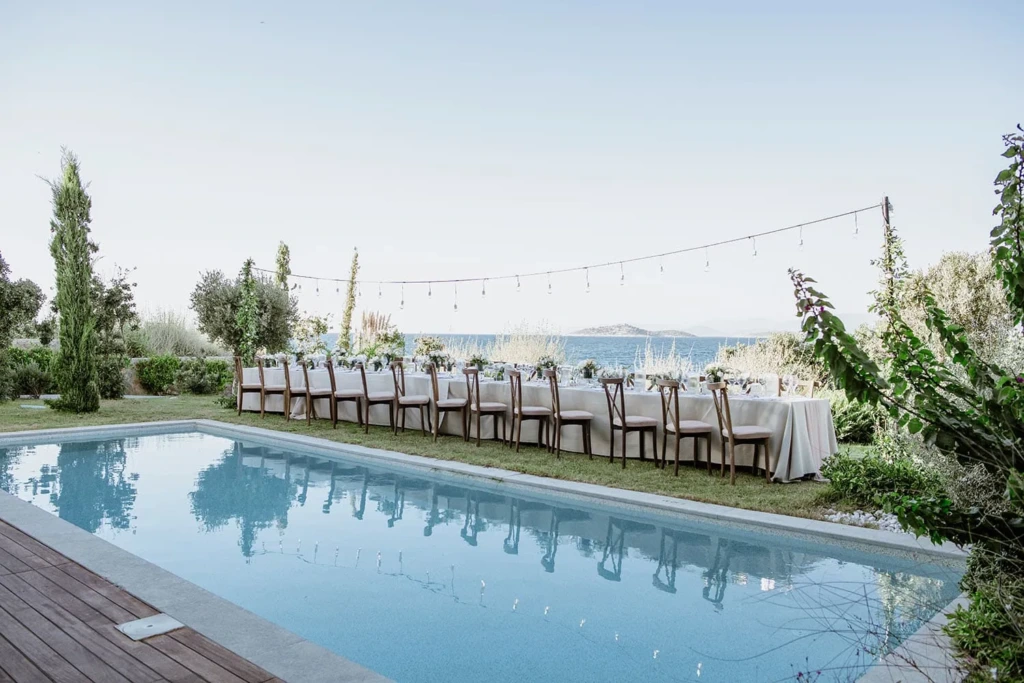 Bodrum'da havuz başında, deniz manzaralı uzun masayla hazırlanan minimalist ve doğal düğün alanı.