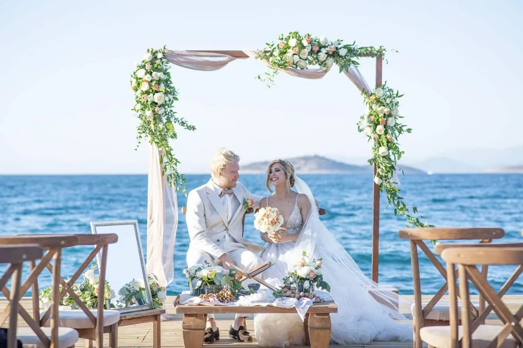 Bodrum’da deniz kenarında çiçekli tag altında gerçekleşen bohem stilde romantik düğün töreni.