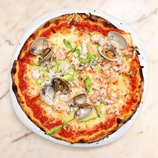 Beyaz mermer bir zeminde beyaz tabakta sunulan, kırmızı domates sosu tabanı üzerinde erimiş mozzarella peyniri, taze açılmış midyeler, bol miktarda pembe karides ve beyaz kalamar parçacıklarıyla süslenmiş, kenarları hafifçe kavrulmuş, otlarla tatlandırılmış bu iştah açıcı deniz mahsullü pizza, İstanbul'un en iyi pizzaları listesindeki iddialı restoranların özgün yorumlarından biri.
