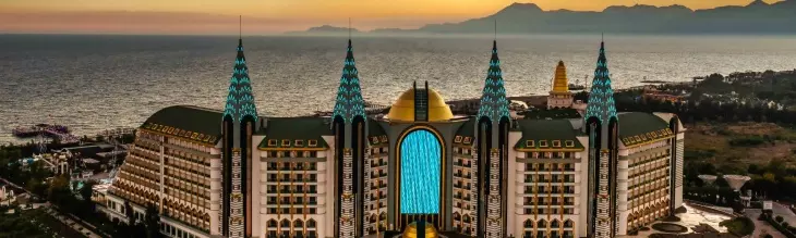 Gün batımının turuncu gökyüzü altında, denize nazır konumlanmış, kendine özgü sivri çatılı ve altın kubbeli görkemli bir mimariye sahip olan bu lüks otel, Türkiye'nin en iyi aile otellerinden biri olarak huzurlu bir tatil vaat ediyor.