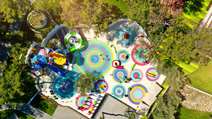Hava fotoğrafında, çok sayıda renkli su kaydırağı ve çocukların eğlenmesi için tasarlanmış, spiral gökkuşağı desenli zeminlere sahip, yemyeşil ağaçlarla çevrili büyük bir aquapark alanı görülüyor, bu da Türkiye'nin en iyi aile otellerinde sunulan eğlenceli tatil deneyimlerine örnek teşkil ediyor.