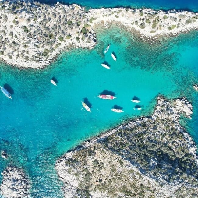 Antalya'nın En Güzel Plajları başlıklı içeriğimizde öne çıkan Akvaryum Koyu'nun kuşbakışı fotoğrafında, çevresindeki kayalık arazilerle çevrili, berrak turkuaz renkteki sularında demirlemiş çok sayıda tekne, adeta gerçek bir akvaryumu andıran doğal güzelliğiyle dikkat çekiyor.