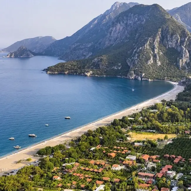 Antalya'nın doğal güzellikleriyle ünlü Çıralı Plajı'nın kuşbakışı görüntüsünde, masmavi denizin kavisli uzun sahili, kıyı şeridini saran yemyeşil ormanlık alan ve arkasındaki heybetli dağlarla bütünleşen turistik yerleşim alanının huzurlu atmosferi dikkat çekiyor.