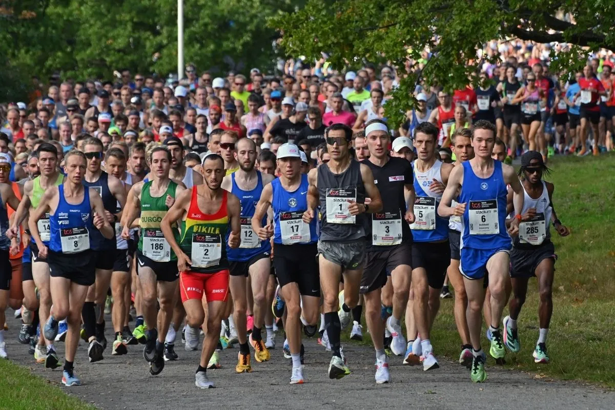 Çeşitli spor kıyafetleri içindeki yüzlerce koşucunun, binalarla çevrili bir şehir caddesinde büyük bir maraton etkinliğine yoğun bir şekilde katıldığını gösteren geniş bir çekim; bu görüntü dünyanın en ünlü maratonlarının ruhunu ve ölçeğini mükemmel bir şekilde yakalıyor.