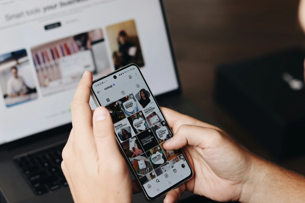 Bir kişi elinde akıllı telefonla Instagram'da bir işletme hesabının iş stratejileri, finansal okuryazarlık ve iş kurma fikirleri içeren gönderilerini inceliyor, bu da en çok kazanan Instagram hesaplarının içeriklerine bir gönderme yapıyor.