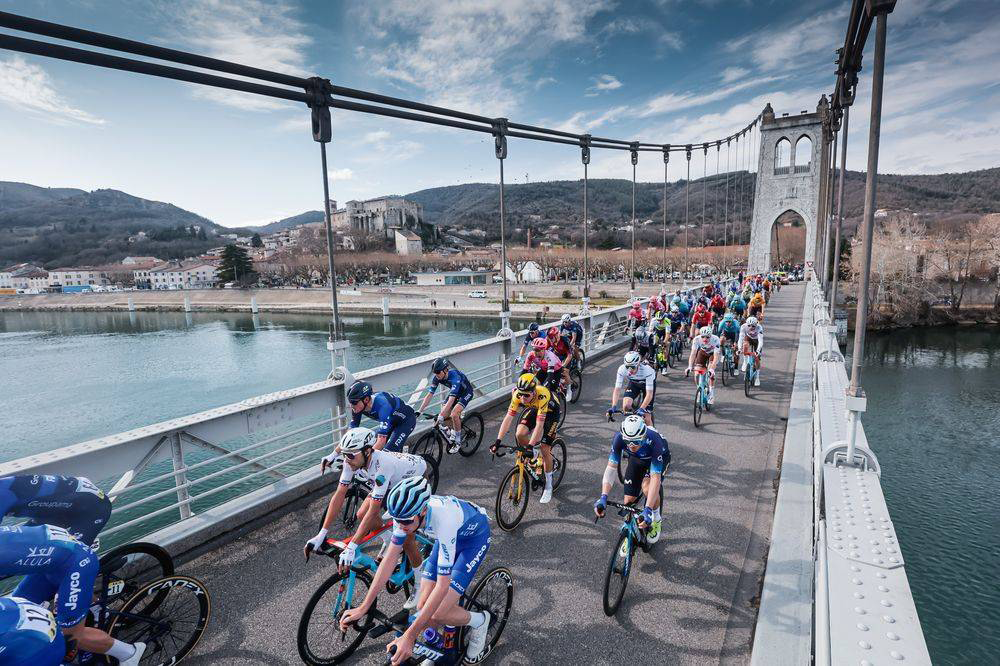 Renkli formalar giymiş onlarca bisikletçi, mimarisiyle dikkat çeken büyük bir asma köprü üzerinde, nehir boyunca uzanan tarihi bir kasabanın ve yemyeşil tepelerin eşlik ettiği Paris-Nice gibi dünyanın en ünlü bisiklet yarışlarından birinde hızla ilerliyor.