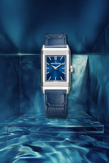 Derin lacivert kadranı ve kayışıyla öne çıkan ikonik dikdörtgen kasalı Jaeger-LeCoultre Reverso kol saati, su yüzeyinin dinginliğini yansıtan mavi bir zeminde sergilenerek, rengini denizden alan şık lacivert saat modellerinin zarafetini vurguluyor.