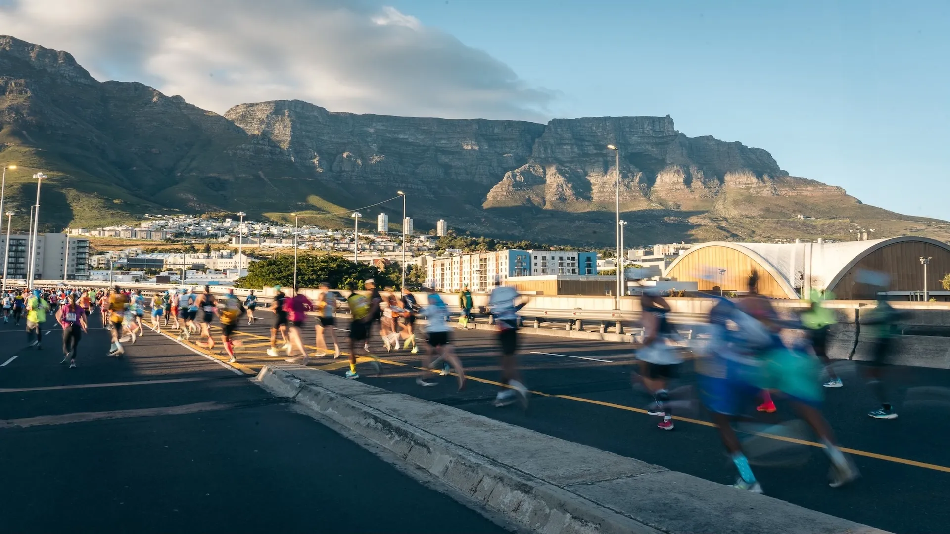 Sanlam Cape Town Maratonu'nda, rengarenk spor kıyafetleri içindeki yüzlerce katılımcı, güneşin altında Cape Town şehrinin tarihi yapıları ve doğal güzelliklerinin eşlik ettiği parkurda coşkuyla koşarak unutulmaz bir deneyim yaşarken, bu büyük etkinliğin heyecanını gözler önüne seriyor.
