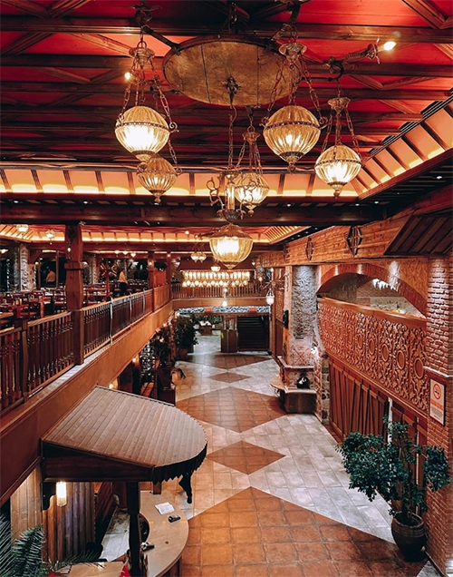 Kayseri'nin en beğenilen restoranlarından Taşmekan Et Lokantası'nın, ahşap kirişler ve kırmızı panellerle kaplı yüksek tavanından sarkan göz alıcı küresel avizelerle aydınlanan, tuğla ve ahşap detaylarla bezeli, çok katlı, desenli zeminli ve sıcak atmosferli geniş iç mekanı.