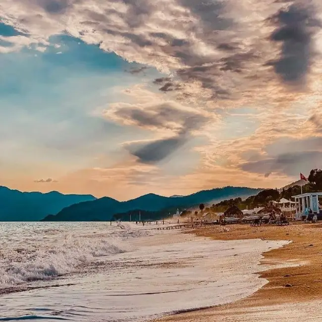 Antalya'nın Kemer ilçesindeki Tekirova Plajı'nda gün batımı veya doğumu, altın renkli kumları, sahile vuran beyaz köpüklü dalgaları ve çam ağaçlarıyla kaplı dağların gölgesinde uzanan turistik tesisleri gözler önüne seriyor.
