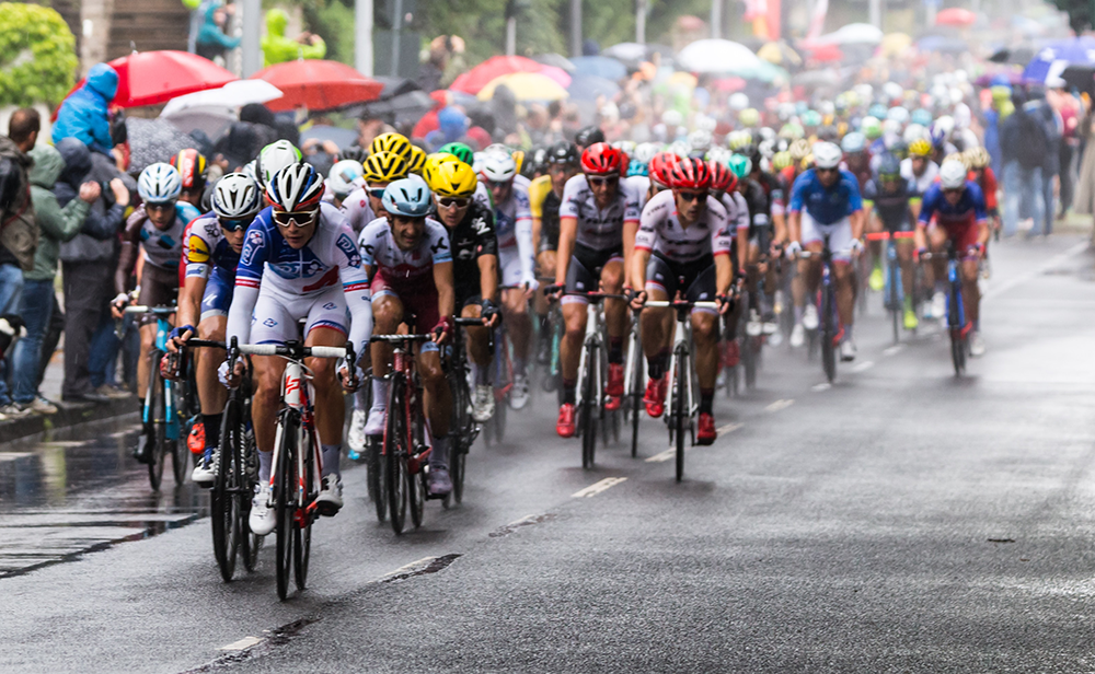 Yağmurlu bir havada, ıslak asfaltta renkli formalarıyla pedallayan kalabalık bir profesyonel bisikletçi grubu, Tour de France gibi dünyanın en ünlü bisiklet yarışlarının çekişmeli ve nefes kesen anlarını gözler önüne seriyor.