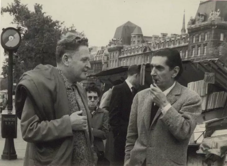 Siyah beyaz bu fotoğrafta, ressam Abidin Dino sol profilden gülümseyerek karşısındaki arkadaşıyla hararetli bir sohbete dalmışken, sağdaki arkadaşı ağzında piposuyla düşünceli bir ifadeyle ona bakıyor, arka planda ise Paris'in tipik çatıları ve kitapçı tezgahları seçiliyor.