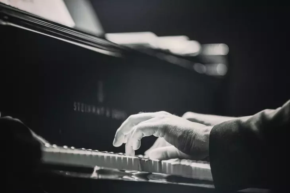 Siyah beyaz tonlarda, koyu bir arka planda dramatik bir ışıkla aydınlatılmış bu yakın çekimde, bir piyano üzerinde müzik çalan eller belirgin bir şekilde görülüyor; grand piyanonun tuşlarına uzanmış parmakların ve hafifçe seçilen Steinway logosunun öne çıktığı görüntü, Frederic Chopin'in müziğine gönderme yapıyor.