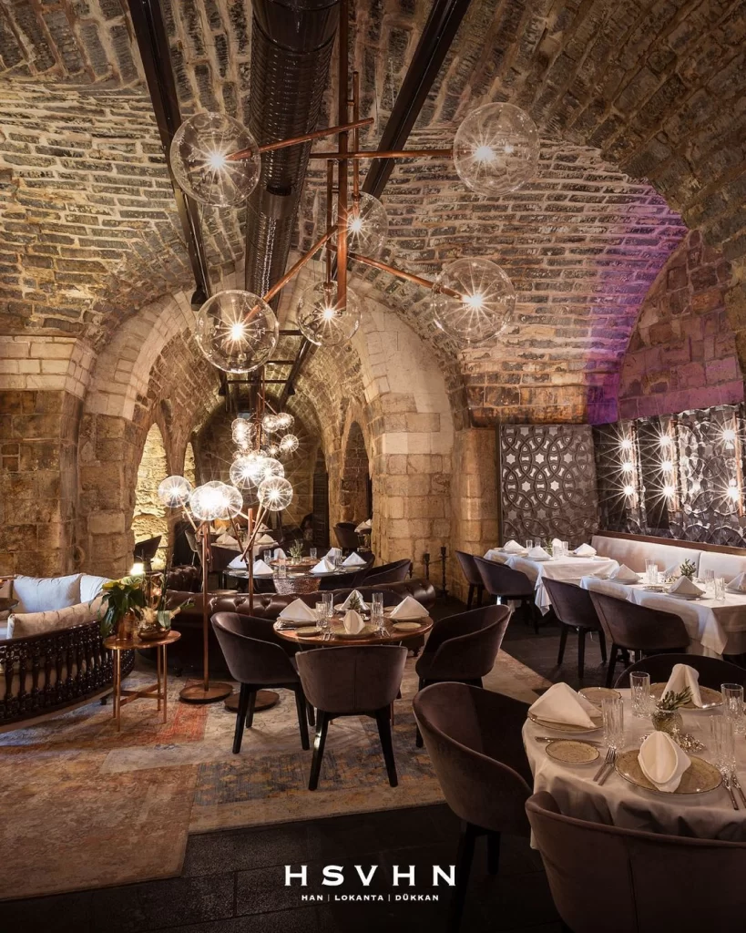 Tarihi taş kemerlerin altında şık dekorasyonu ve zarif masa düzeniyle HSVHN restoran bölümü.