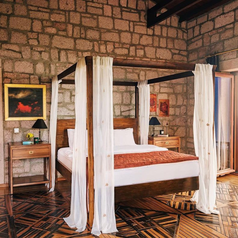 Simurg Inn’in taş duvarlı odasında tül detaylı karyola ve otantik dekorasyon ile konforlu konaklama