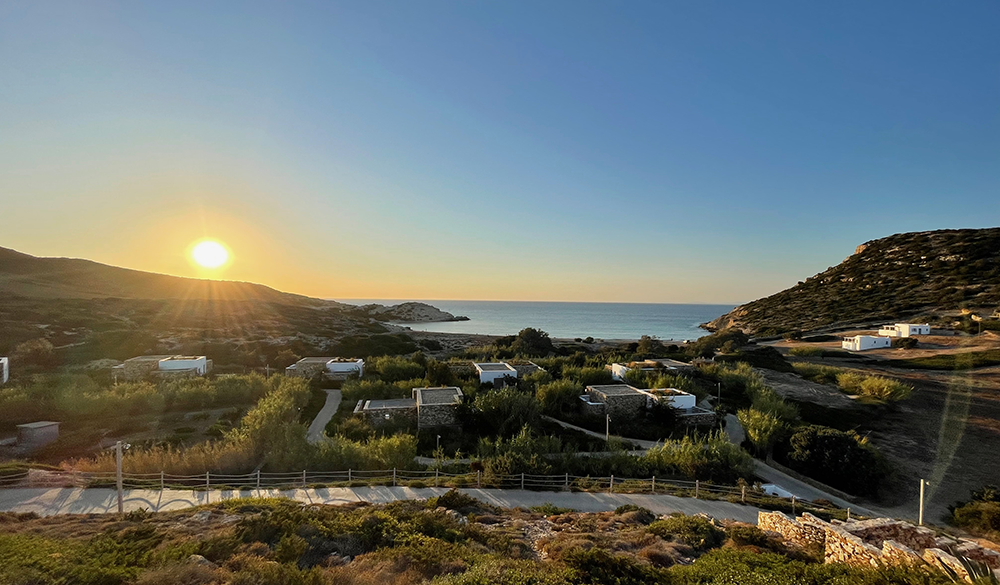 Paros seyahat rehberi kapsamında Antiparos'un bakir Livadia Koyu'nda yer alan, doğal taş mimarisiyle çevreye uyumlu villaların deniz kıyısında gün batımının kızıl ve altın rengi ışıkları altında huzurlu bir atmosfer sunduğu geniş bir genel görünüm.
