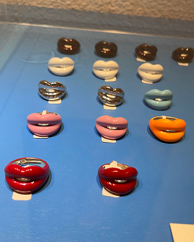 Mavi bir yüzey üzerinde sergilenen, kırmızı, pembe, turuncu, açık mavi, beyaz ve kahverengi tonlarında, Solange'nin Hot Lips serisinden dudak şeklinde birçok yüzük, Paros seyahat rehberinde yer alan lüks mücevher seçeneklerini vurguluyor.