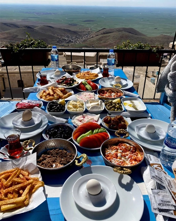 Mardin'in nefes kesen vadi manzarasına hakim bir balkonda, mavi beyaz çizgili bir masada serili, kızarmış patates, haşlanmış yumurta, siyah ve yeşil zeytinler, peynir çeşitleri, menemen ve kıymalı yumurta gibi onlarca lezzetli yiyeceğin bulunduğu zengin bir Türk kahvaltısı.