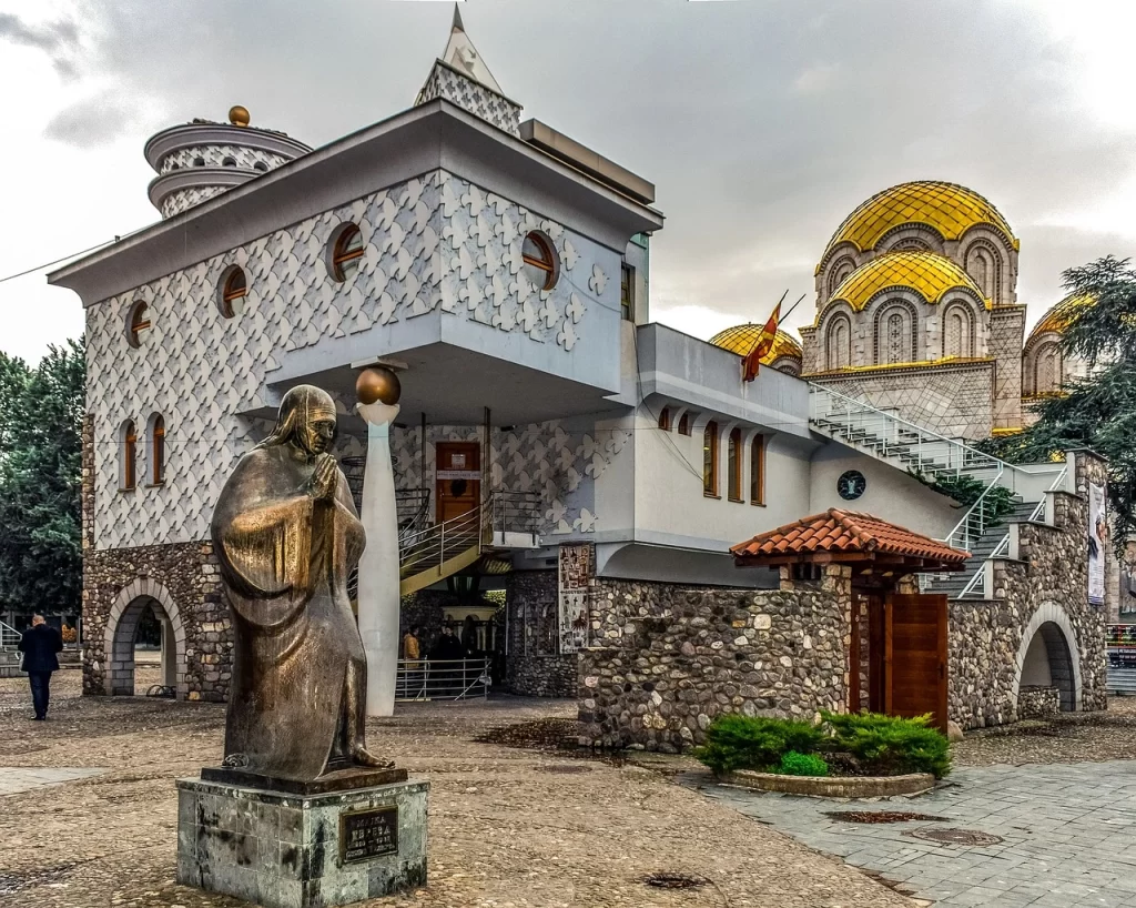 Üsküp'te görmeniz gereken en özel yerlerden biri olan Rahibe Teresa Evi'nin önündeki Rahibe Teresa heykeli ve arka planda altın kubbeleriyle Aziz Ohrili Klement Katedrali'nin bir arada görüldüğü bu görüntü, Balkan şehrinin kültürel zenginliğini vurguluyor.