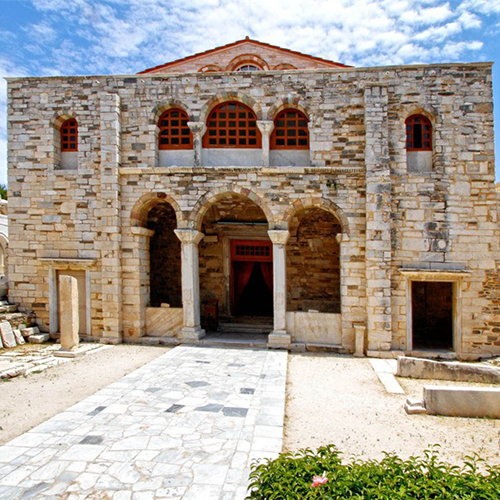 Paros'un tarihi dokusunu yansıtan, taş cepheli, kemerli pencereleri ve kırmızı çatısıyla dikkat çeken, '99 kapılı' olarak bilinen Panagia Ekatontapiliani Kilisesi'nin görkemli dış cephesi, Paros seyahat rehberi içeriğiyle uyumlu, ikonik bir ziyaret noktası.