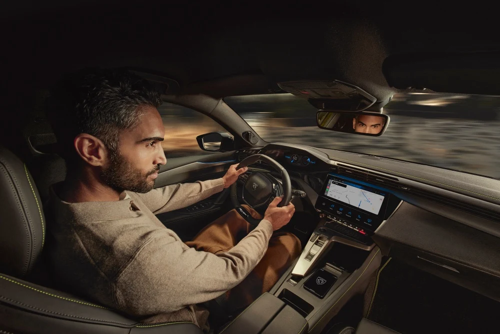 Peugeot 408'in modern iç mekanında, direksiyonu tutan sakallı bir erkek sürücü, dijital i-Cockpit gösterge panelinden hızı (50 km/s) takip ederken, navigasyonlu geniş multimedya ekranının sunduğu sezgisel sürüş deneyiminin keyfini çıkarıyor.