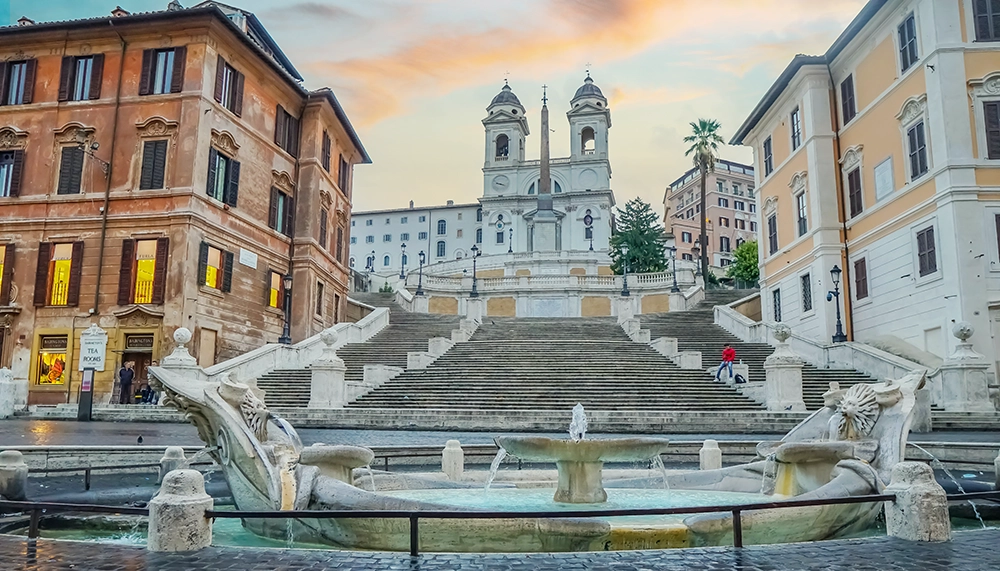 Görkemli İspanyol Merdivenleri, tepesindeki Trinità dei Monti Kilisesi ve önündeki Bernini'nin Barcaccia Çeşmesi ile Roma seyahatinizin unutulmaz duraklarından biri olan bu tarihi ve sanatsal yapıyı gün batımı kızıllığında huzurlu bir an sunarken gösteriyor.