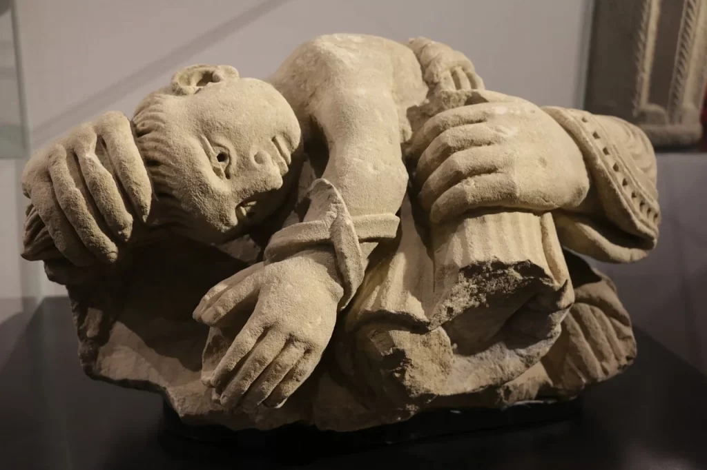 Üsküp Arkeoloji Müzesi koleksiyonundan, açık renkli, yıpranmış dokulu taştan oyulmuş, başı eğik, elleri bedene kenetlenmiş, gergin bir duruş sergileyen antik bir figürün parçası, şehrin derin tarihini gözler önüne seriyor.