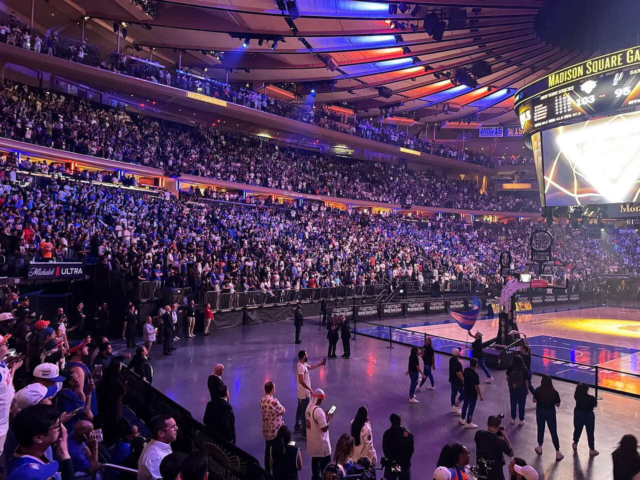 Madison Square Garden'da, tavanındaki kırmızı ve mavi ışıkların aydınlattığı tıklım tıklım dolu tribünlerdeki binlerce coşkulu taraftarın tezahürat yaptığı ve dev skorboardda New York Knicks ile San Antonio Spurs arasındaki NBA maçının heyecanını yansıtan, NBA Finallerine yakışır görkemli bir sahne.