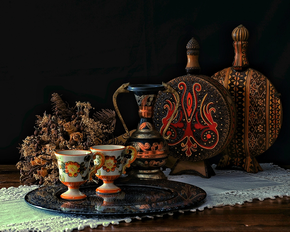  Siyah fon önünde kurutulmuş çiçekler, geleneksel motifli sürahiler, tahta dekoratif eşyalar ve çiçek desenli fincanlarla hazırlanmış nostaljik bir sofra düzeni.