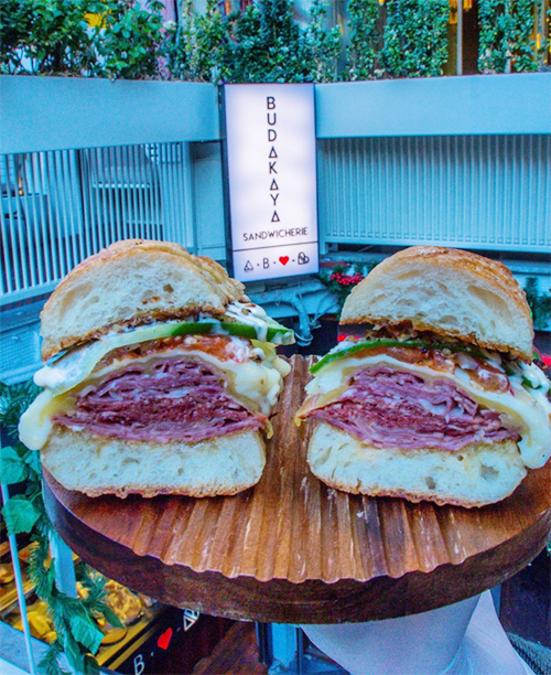 Budakaya Sandwicherie'den kalın dilim et, erimiş peynir ve taze yeşilliklerle dolgunlaştırılmış, özel ekmekler arasında sunulan iki sandviç yarımı, Bebek'in en iyi mekanları listesindeki bu özgün sandviç dükkanının farkını ortaya koyuyor.