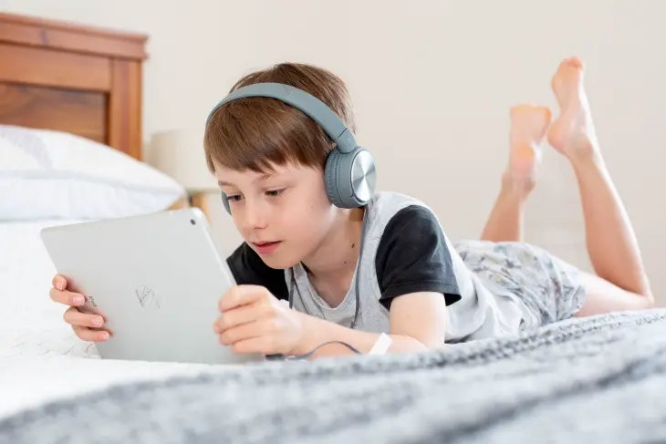 Kulaklıkla tablet üzerinden interaktif eğitim oyunları oynayan çocuk.