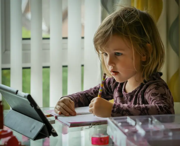 Tablet eşliğinde not alarak dijital öğrenme sürecine katılan okul öncesi çocuk.