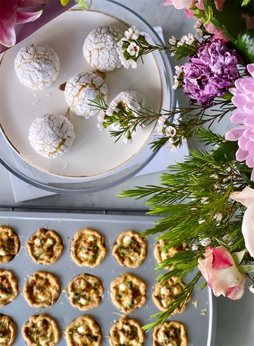 “Healthy Bakery’de hazırlanan katkısız fırın lezzetleri: pudra şekerli kurabiyeler ve mini kişler, taze çiçeklerle süslenmiş bir sunumla.”