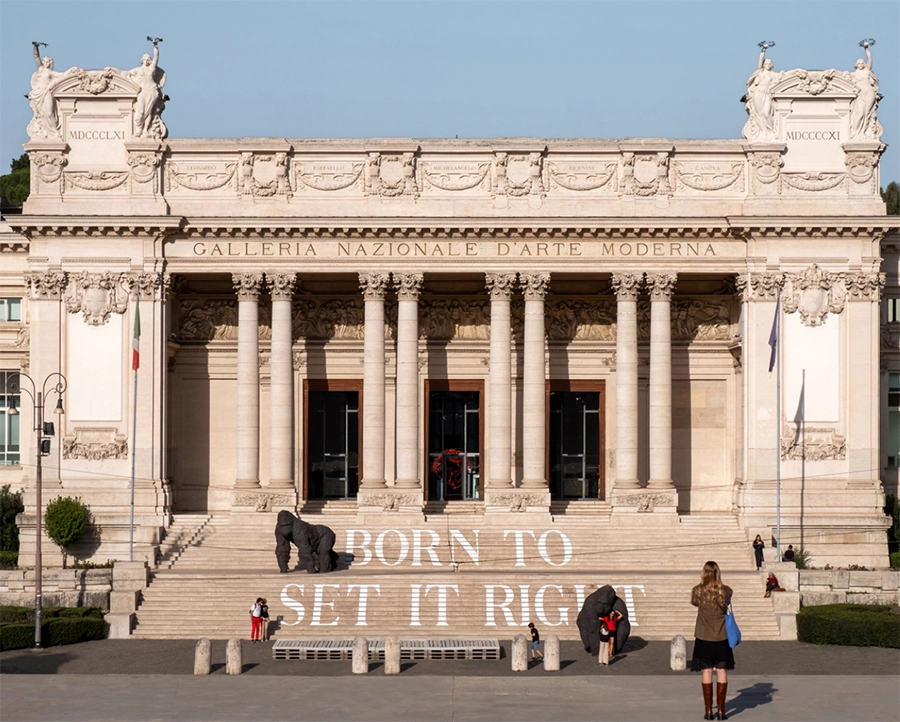 Roma Seyahat Rehberi içinde önemli bir sanat durağı olan La Galleria Nazionale d’Arte Moderna e Contemporanea'nın görkemli sütunlu ve heykelli cephesi, geniş merdivenlerinde yer alan 'BORN TO SET IT RIGHT' yazısı ve soyut heykellerle birlikte güncel sanatın Roma'daki dinamik varlığını sergiliyor.