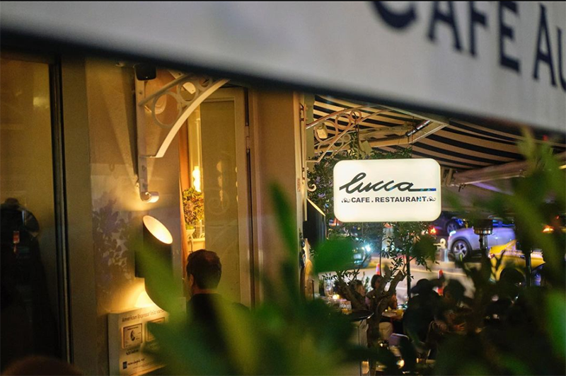 Gece çekilmiş bu fotoğrafta, Bebek'in en gözde buluşma noktalarından biri olan Lucca Cafe Restaurant'ın aydınlatılmış tabelası, çizgili tentesinin altındaki kalabalık müşteri alanı ve etraftaki yeşillikler, mekanın canlı ve davetkar atmosferini yansıtıyor.