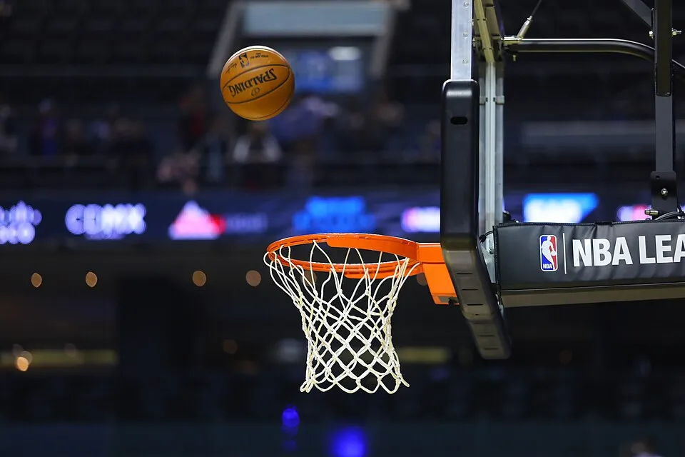 Yoğun bir NBA maçında turuncu çemberli ve beyaz fileli potaya doğru alçalan Spalding marka basketbol topu, heyecan dolu bir anı ve basketbol oyunundaki sayının kazanılma anını gösteriyor, bu da NBA kurallarının sahada nasıl işlediğini vurguluyor.