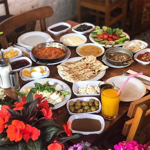 Van Kahvaltı Evi’nde otlu peynir, bal, kaymak ve sıcak kahvaltılıklarla donatılmış masa.