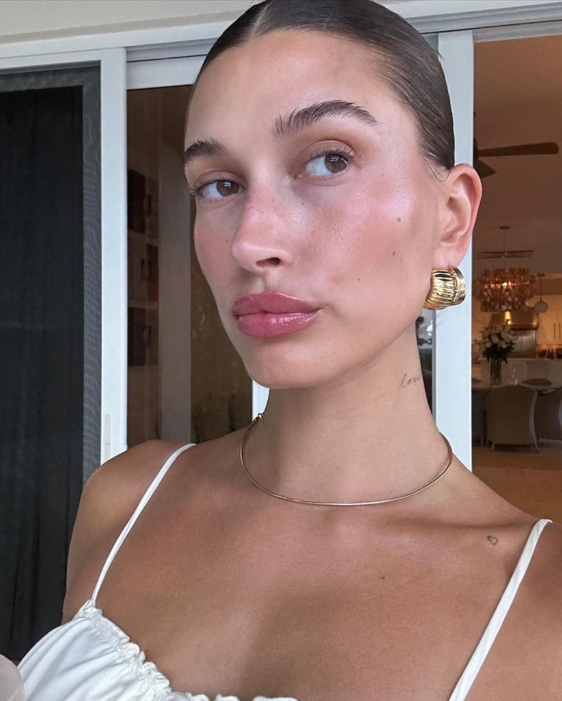 Ayrıca Hailey Bieber olarak da bilinen bu kadın, parlak ten makyajı, pembe parlak dudakları, geriye taranmış saçları ve minimalist altın takılarıyla Vanilla Girl estetiğinin sağlıklı, doğal ve ışıltılı güzellik anlayışını modern bir şekilde yansıtıyor.