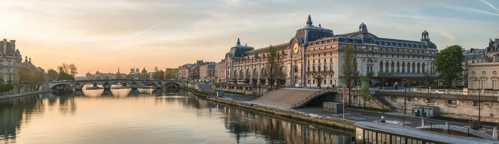 Seine Nehri üzerinde gün batımı ışığında parıldayan tarihi Musée d'Orsay binası, solunda kemerli Pont Royal köprüsü ve nehre yansıyan sakin ve sıcak tonlarla Paris'in büyüleyici güzelliğini gözler önüne seriyor.