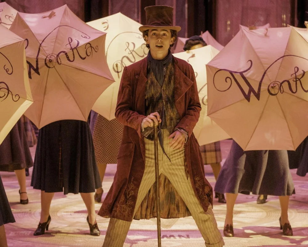 Aralık ayında vizyona girecek Wonka filminin büyülü bir sahnesinde, genç Willy Wonka'yı canlandıran Timothée Chalamet, şık şapkası, uzun bordo paltosu ve bastonuyla, üzerinde büyük harflerle Wonka yazılı, açık renkli şemsiyeler taşıyan kalabalığın ortasında şaşkınlıkla etrafa bakıyor.